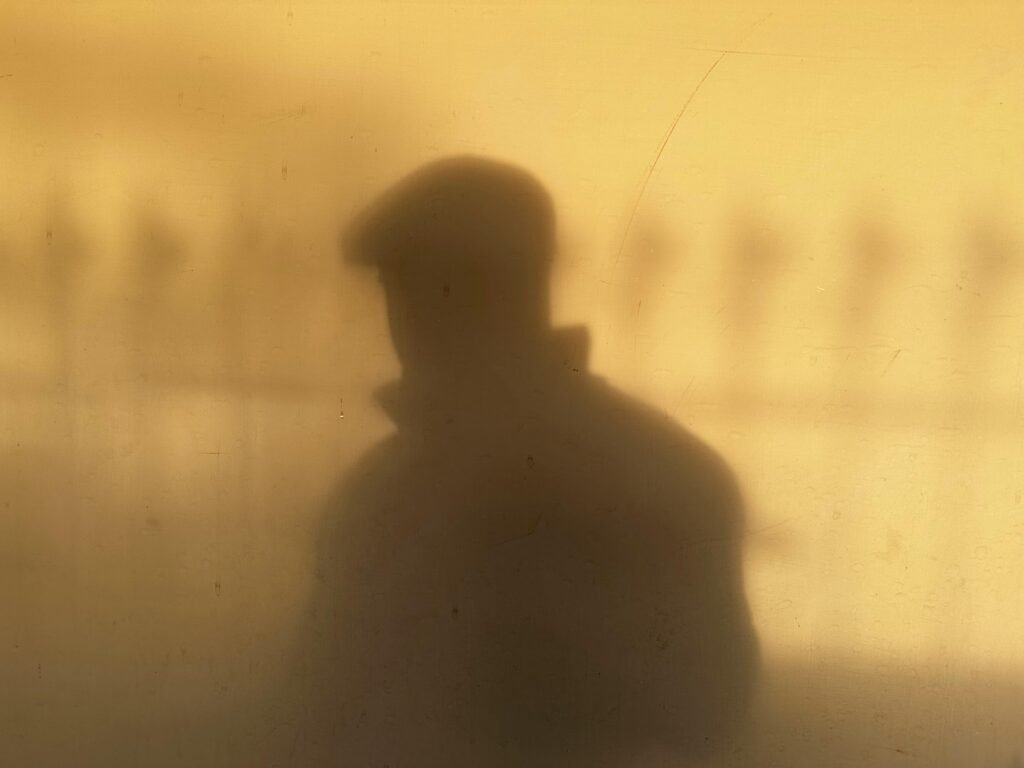A shadow of a man wearing a cap against a warm-toned wall, creating a mysterious silhouette.