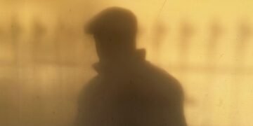 A shadow of a man wearing a cap against a warm-toned wall, creating a mysterious silhouette.